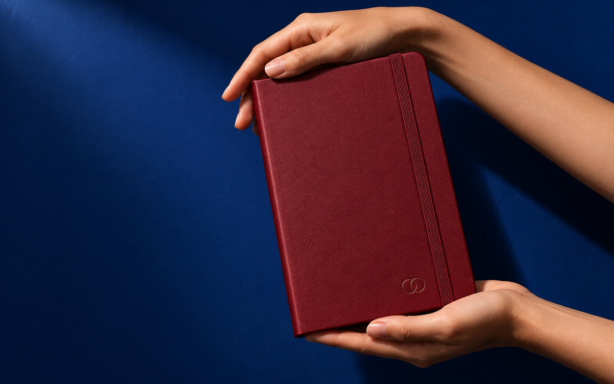 Two hands presenting an Infinote notebook with a small debossed mark on its cover